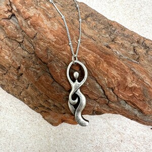 Pu&ograve; includere: Una collana d'argento con un ciondolo a forma di figura femminile stilizzata. Il ciondolo &egrave; astratto e presenta un design fluido e organico.