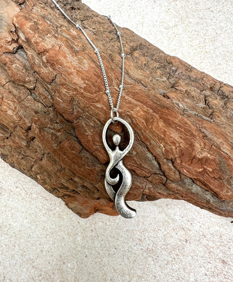 Pu&ograve; includere: Una collana d'argento con un ciondolo a forma di figura femminile stilizzata. Il ciondolo &egrave; astratto e presenta un design fluido e organico.