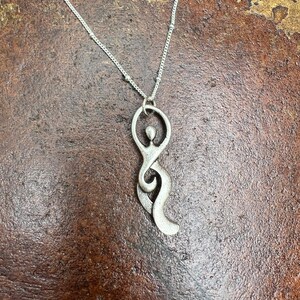 Pu&ograve; includere: Una collana d'argento con un ciondolo a forma di figura femminile stilizzata. Il ciondolo &egrave; astratto e ha un design fluido e organico.