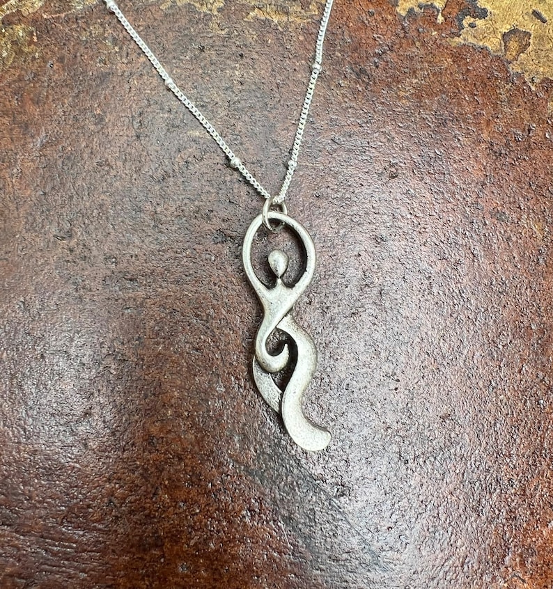 Pu&ograve; includere: Una collana d'argento con un ciondolo a forma di figura femminile stilizzata. Il ciondolo &egrave; astratto e ha un design fluido e organico.