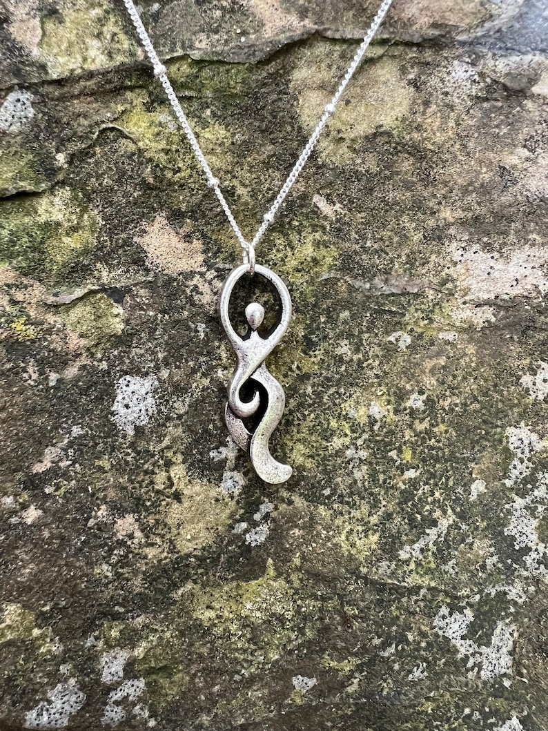 Pu&ograve; includere: Una collana d'argento con un ciondolo che rappresenta una figura umana stilizzata. Il ciondolo &egrave; un design semplice e astratto con una testa circolare e un corpo fluido.