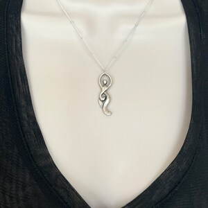 Pu&ograve; includere: Una collana d'argento con un ciondolo a forma di figura femminile stilizzata. Il ciondolo &egrave; testurizzato e ha un aspetto leggermente invecchiato.