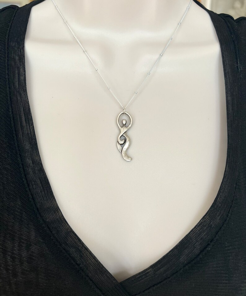 Pu&ograve; includere: Una collana d'argento con un ciondolo a forma di figura femminile stilizzata. Il ciondolo &egrave; testurizzato e ha un aspetto leggermente invecchiato.