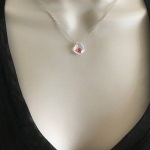 May include: A silver chain necklace with a clear iridescent teardrop-shaped pendant.