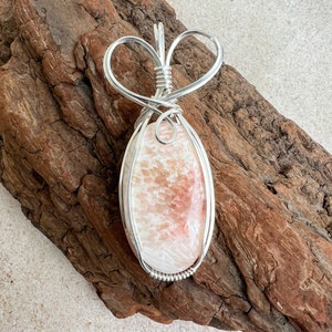 May include: A silver wire wrapped pendant featuring a pink and white oval shaped stone with a heart shaped bail.