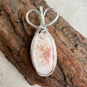 May include: A silver wire wrapped pendant featuring a pink and white agate stone. The pendant is shaped like a heart and has a delicate design.