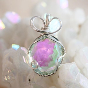 May include: A silver wire wrapped pendant featuring a iridescent green and pink gemstone. The pendant is displayed on a bed of white crystals.