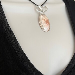 May include: A silver wire wrapped pendant necklace featuring a light brown and white stone with a heart-shaped bail.