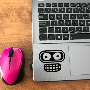 May include: A black and white robot sticker on a silver laptop. The robot has two large eyes and a wide mouth.