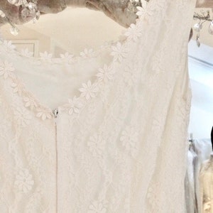 May include: White lace sleeveless top with a delicate floral pattern. The top has a zipper closure in the back.