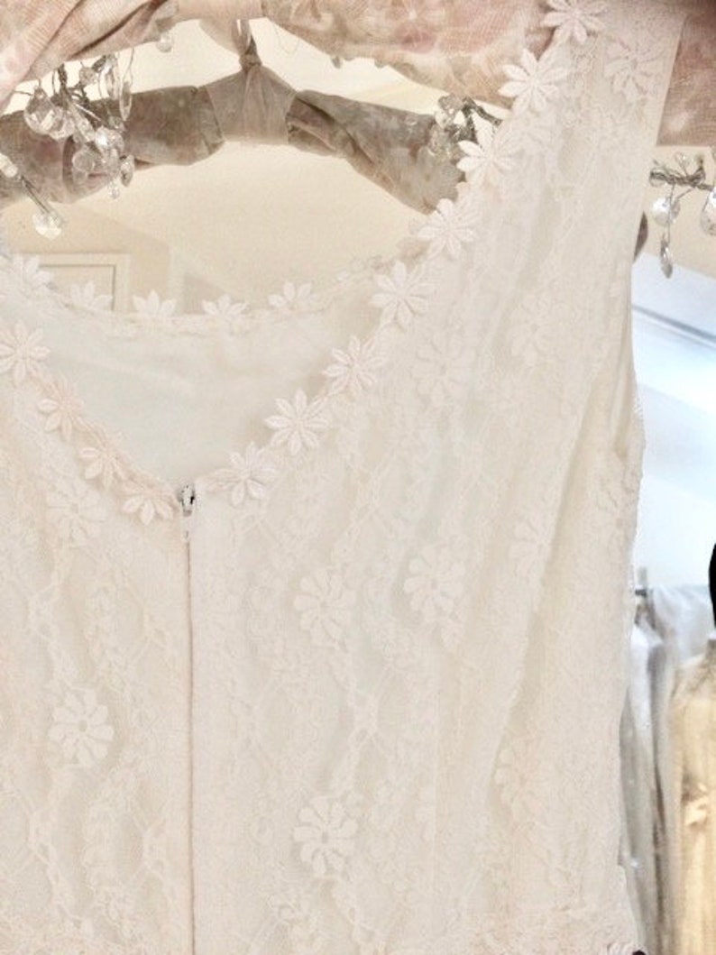 May include: White lace sleeveless top with a delicate floral pattern. The top has a zipper closure in the back.