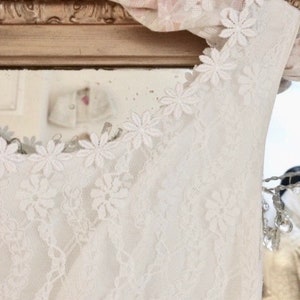May include: White lace sleeveless top with a scalloped neckline and floral lace trim. The lace is delicate and intricate, with a soft, feminine feel.