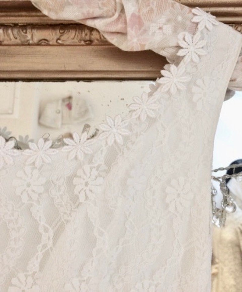 May include: White lace sleeveless top with a scalloped neckline and floral lace trim. The lace is delicate and intricate, with a soft, feminine feel.