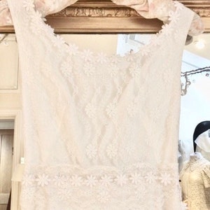 May include: A white lace wedding dress with a fitted bodice and a flowing skirt. The dress is decorated with delicate floral embroidery.