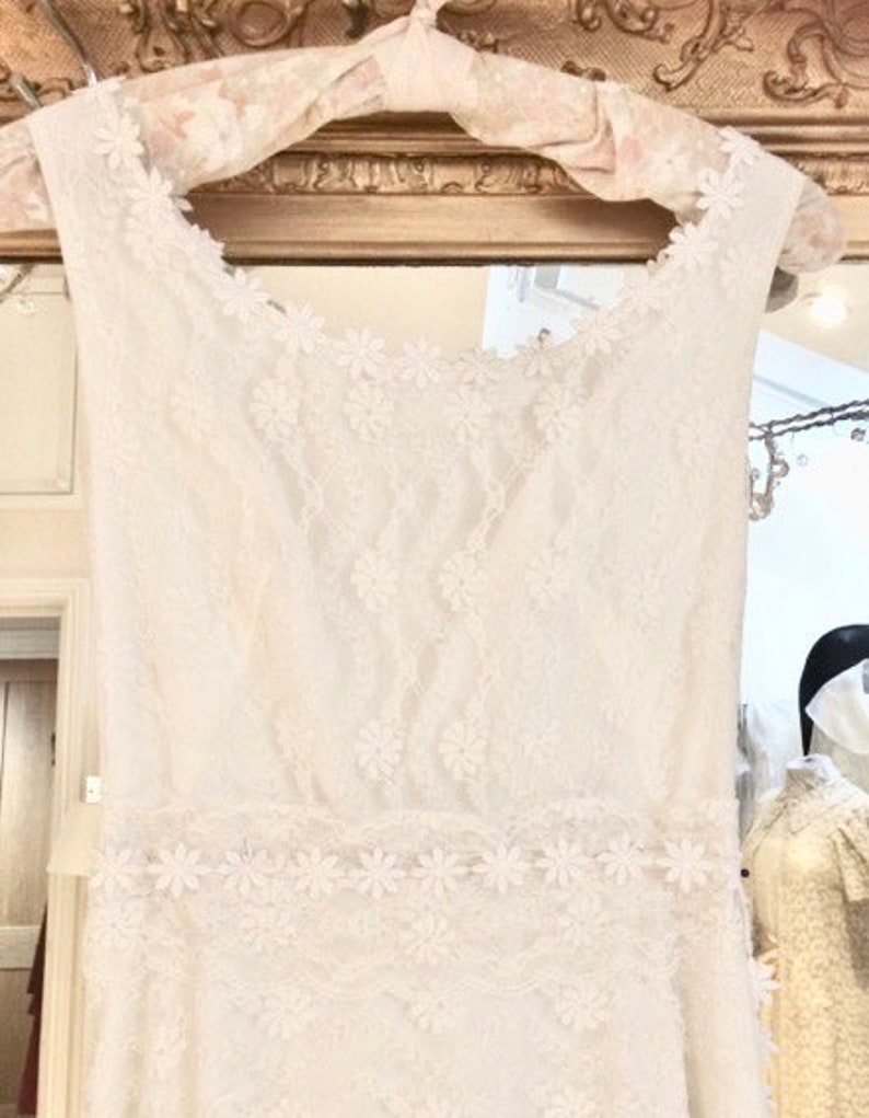 May include: A white lace wedding dress with a fitted bodice and a flowing skirt. The dress is decorated with delicate floral embroidery.