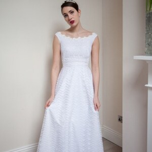 May include: A white lace wedding dress with a scoop neckline and a full skirt. The dress has a fitted bodice and a lace trim around the neckline and sleeves.