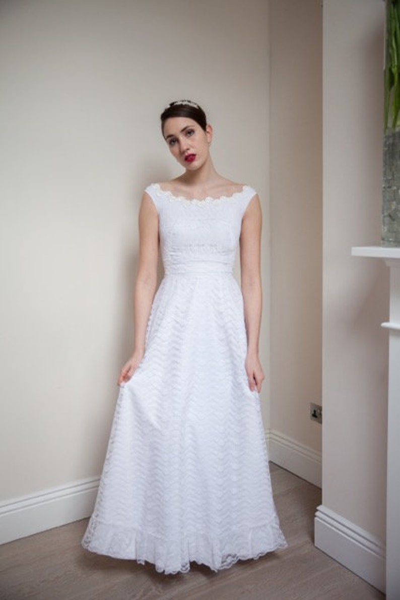May include: A white lace wedding dress with a scoop neckline and a full skirt. The dress has a fitted bodice and a lace trim around the neckline and sleeves.