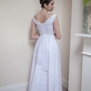 May include: A white lace wedding dress with a scoop neckline and a fitted bodice. The dress has a full skirt and a lace trim at the neckline and hem.
