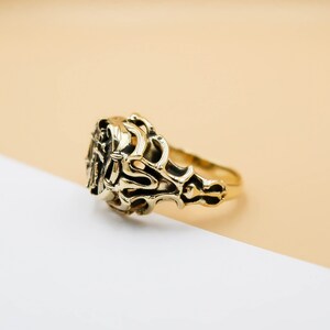 May include: A gold ring with an intricate, ornate design. The ring is made of a single piece of metal and has a smooth, polished finish.
