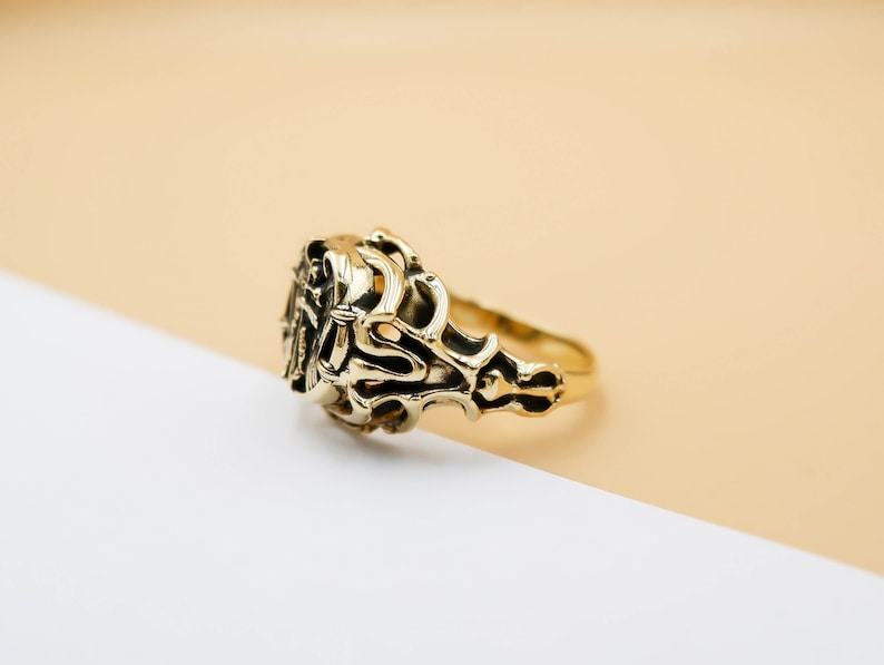 May include: A gold ring with an intricate, ornate design. The ring is made of a single piece of metal and has a smooth, polished finish.