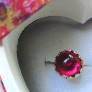 May include: A pair of silver earrings with pink gem stones in a heart-shaped box with a floral pattern.