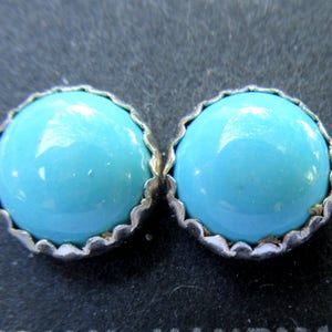 May include: A pair of silver earrings with turquoise stones. The stones are round and have a smooth, polished finish.