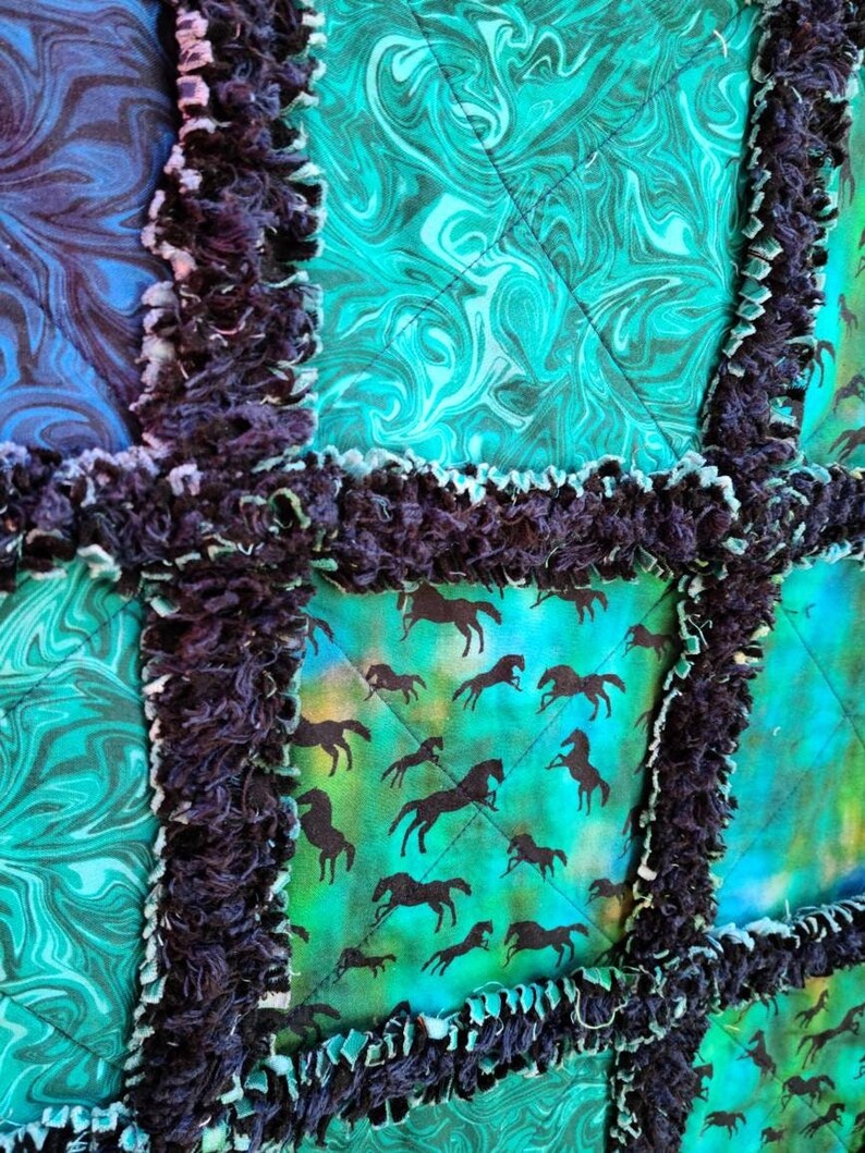 Detailed macro view showing the dark frayed seams separating quilted squares of teal marble and horse-print fabrics.