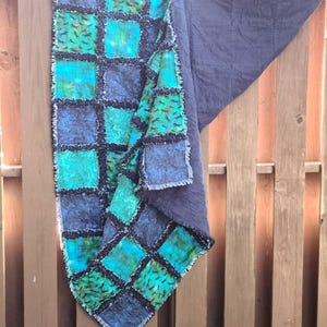 The quilt hangs vertically against a wooden fence with a folded corner revealing the solid dark blue backing fabric.