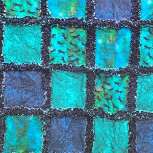 Close-up horizontal section of the quilt showcasing multiple textured blocks in shades of blue and teal green.