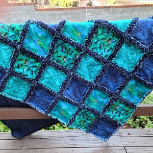 The rag quilt is draped over a wooden railing outdoors, showing its quilted squares and exposed fringed seams.