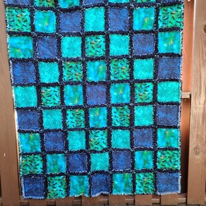 Full shot of the patchwork rag quilt hanging against a wooden fence, displaying a checkered pattern of blue, teal, and horse motifs.