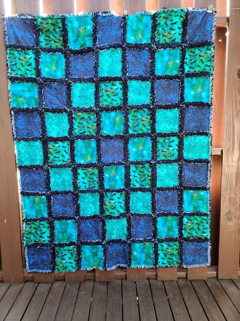 Full shot of the patchwork rag quilt hanging against a wooden fence, displaying a checkered pattern of blue, teal, and horse motifs.
