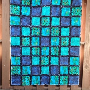 Frontal full view of the handmade rag quilt hung against a wooden backdrop, showing the complete checkerboard layout.