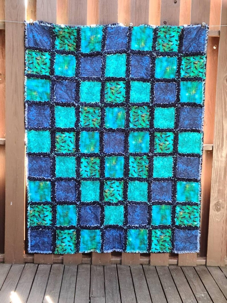 Frontal full view of the handmade rag quilt hung against a wooden backdrop, showing the complete checkerboard layout.