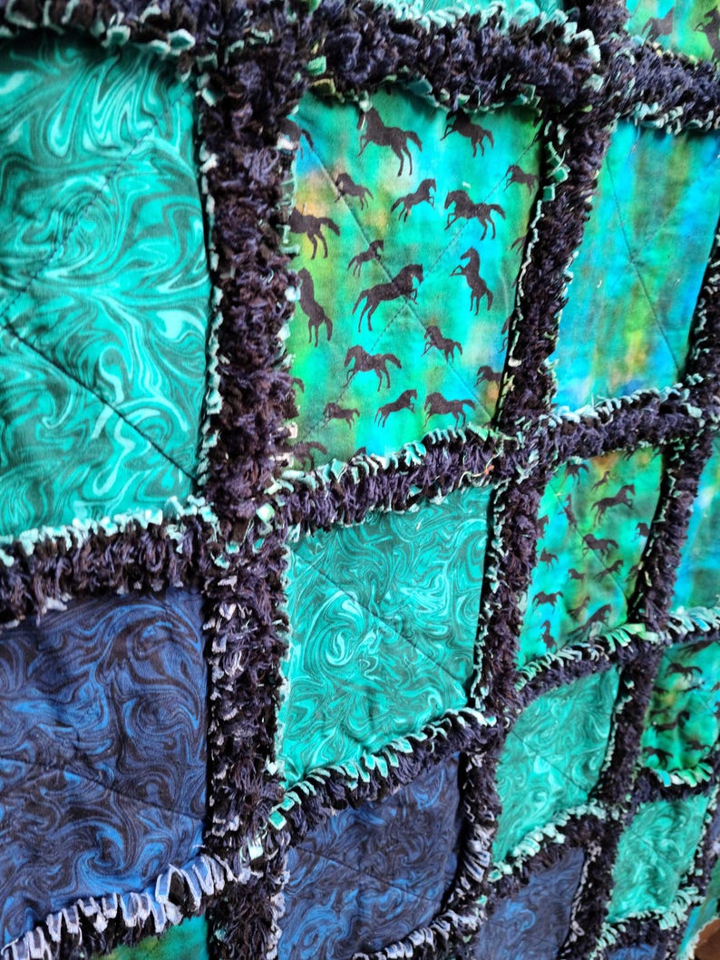 Close-up view of several patchwork squares displaying swirling blue patterns and black galloping horse silhouettes.