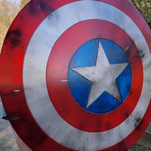 May include: A Captain America shield, featuring a red, white, and blue color scheme. The shield has a central blue circle with a white star, surrounded by concentric white and red bands. The shield has a distressed, battle-worn appearance.