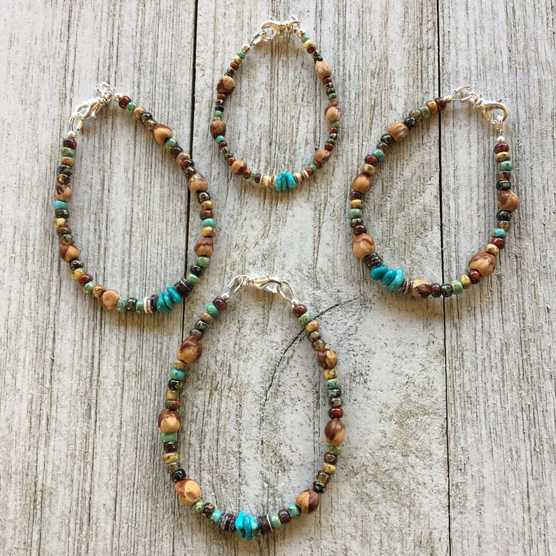 Puede incluir: Tres pulseras de cuentas con cuentas turquesas y marrones. Las pulseras est&aacute;n sobre un fondo de madera blanco.