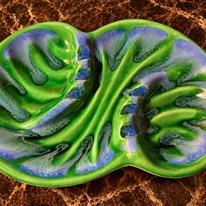 May include: A dual-section ceramic tray featuring a glossy finish with a vibrant green base color and radiating blue glaze patterns that extend from the center toward the edges, creating a distinct organic, leaf-like appearance across the surface.