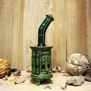May include: Green ceramic incense burner shaped like a small house with a chimney. The burner has intricate floral details and a gold door. The burner is sitting on a wooden surface with various decorative items.