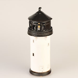 May include: White ceramic lighthouse with a black roof and windows. The lighthouse has a small light inside.