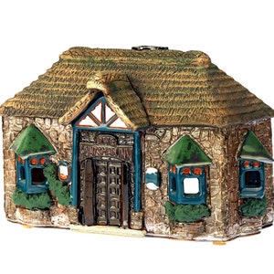 May include: A miniature decorative house with a thatched roof and stone walls. The house features green window awnings, blue window frames, and a dark brown door. The text "THE WATERSIDE" is above the door.