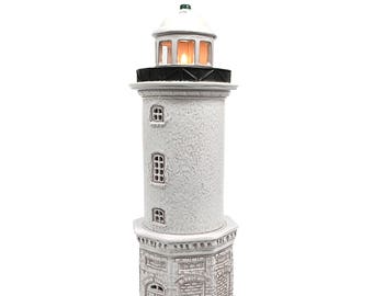May include: White ceramic lighthouse figurine with a black roof and red base. The lighthouse has a small window and a light inside.