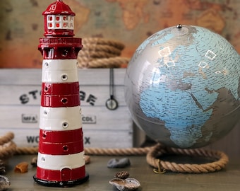 May include: A red and white ceramic lighthouse figurine with a globe in the background. The lighthouse has a black base and a red and white striped body. The globe is blue and silver and has a world map printed on it.