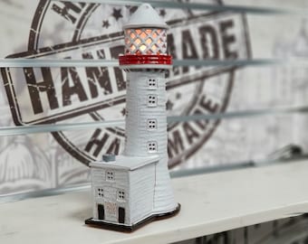May include: White ceramic lighthouse figurine with a red roof and a light inside. The lighthouse has a small building attached to the base with the text "TUDOR ROCK LIGHTHOUSE 1835" on the side.