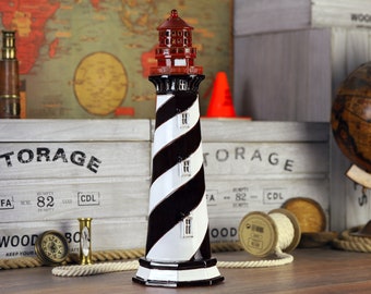 May include: A black and white striped lighthouse figurine with a red roof. The lighthouse is on a wooden surface with a globe, rope, and other nautical decor.