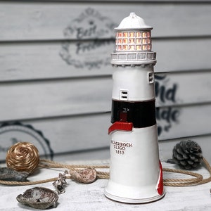 Op de afbeelding: Een keramische vuurtoren met een witte behuizing, zwarte streep en rode accenten. Het bovenste gedeelte heeft een verlichtingsfunctie. De vuurtoren heeft de tekst "Blackrock Sligo 1819". Het wordt gepresenteerd op een wit dienblad met decoratieve items.