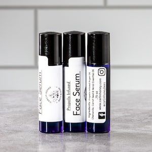 May include: Three small blue glass bottles with black roll-on tops. The bottles are labeled "Face Serum" and "Propolis Infused Face Serum". The labels also include the brand name "Carlin Honey" and the website address "www.carlinhoney.com".