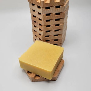 May include: A stack of wooden soap dishes with a yellow bar of soap on top of one of the dishes.