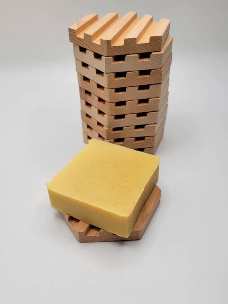 May include: A stack of wooden soap dishes with a yellow bar of soap on top of one of the dishes.