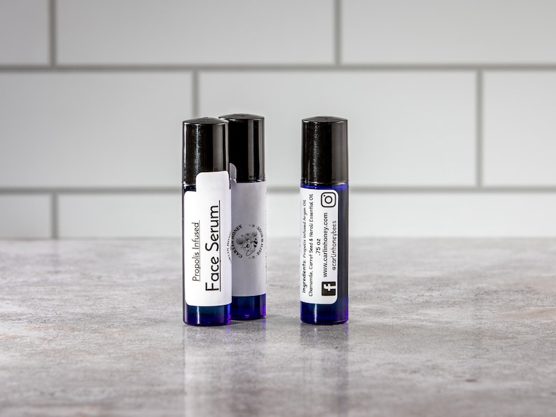 May include: Three blue glass roller bottles with white labels. The labels read "Propolis Infused Face Serum" and include the brand name "Carlin Honey" and social media icons.